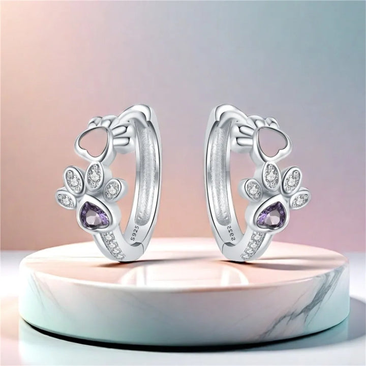 Silver paw print earrings with zirconia and a heart-shaped gemstone.
